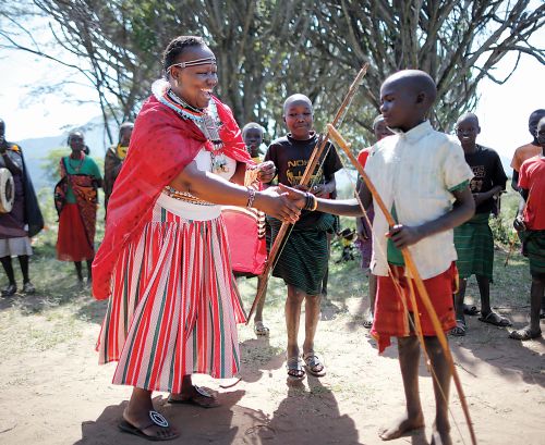 Η δασκάλα των Ποκότ με την επίσημη ενδυμασία της συγχαίρει ένα από τα αγόρια που κέρδισε σε παιχνίδι τοξοβολίας