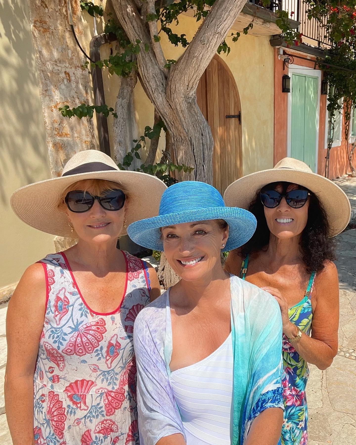 Actress Jane Seymour wearing a blue hat white bathing suit and a multicolored wrap sarong. She is in the middle between her two sisters Annie on the left is wearing a floral dress sun hat