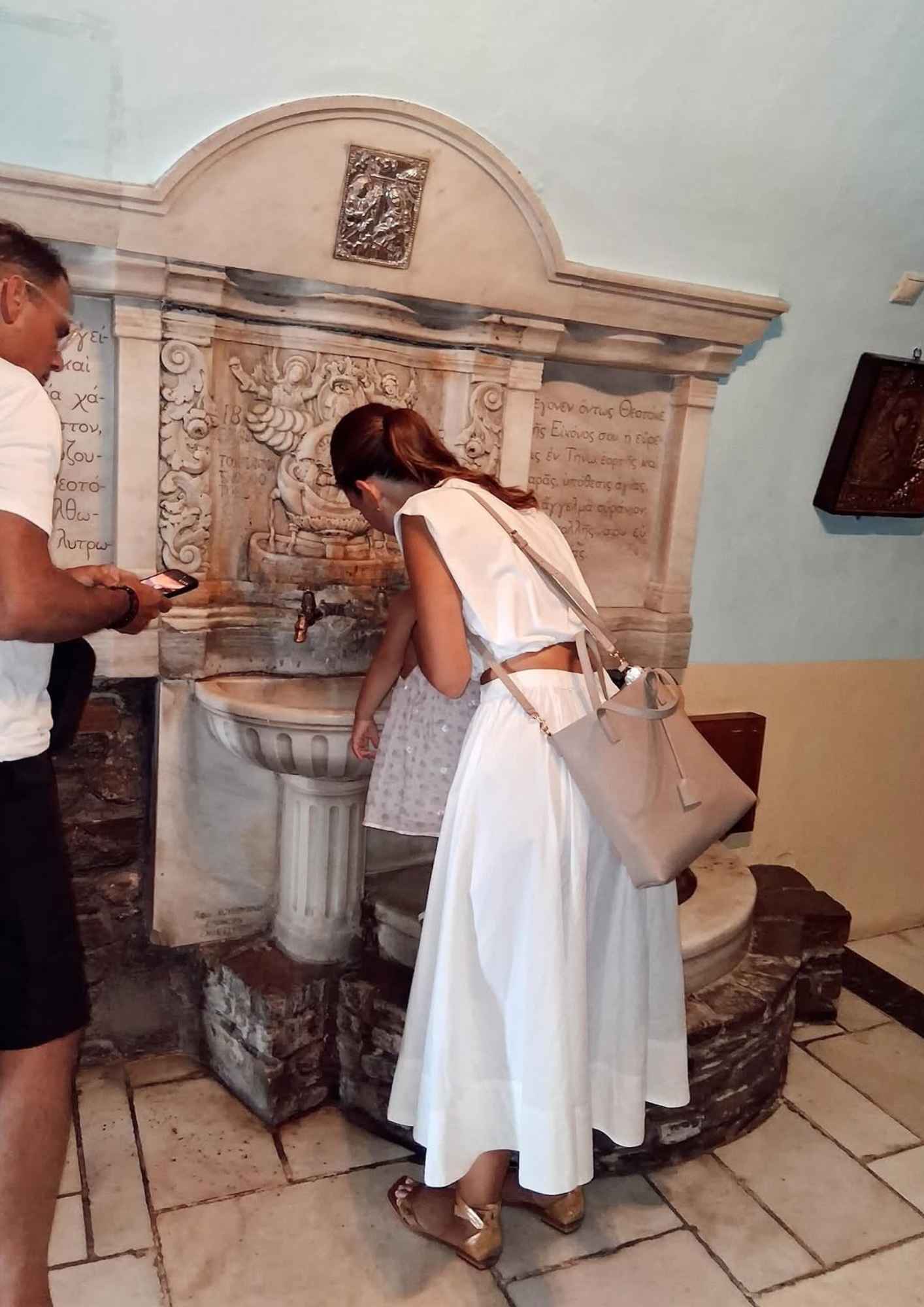 Η Μαρία Μενούνος με την κόρη της σε κρήνη του προσκυνήματος στην Τήνο